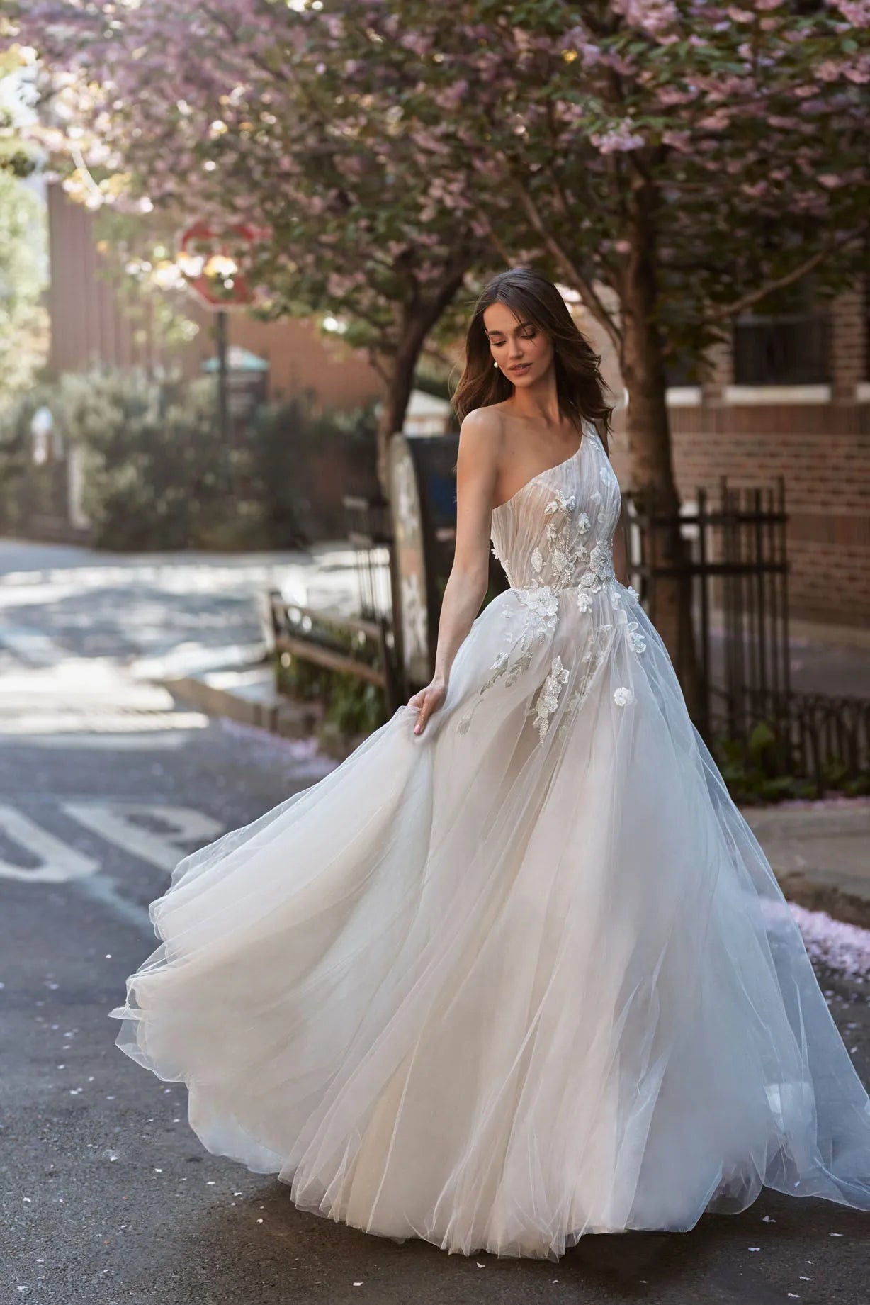 Expremely feminine and fragile wedding gown. The top is embellished with the scrunched up Tulle and floral elements that cover one shoulder. The skirt is made of numerous layers of Tulle with accentuated waistline and 3D floral lace.