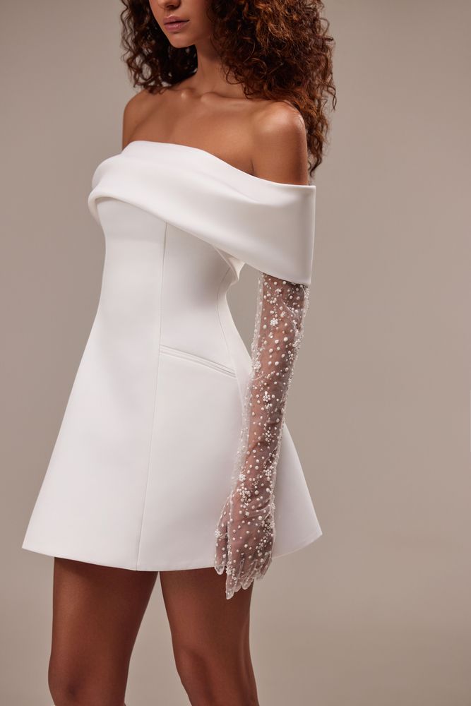 Showstopper mini wedding dress cut from satin. The sleeveless design features a straight neckline and a snatched waist that flows into a mini skirt. Can be complemented with an off-the-shoulder satin bolero with sheer long sleeves embellished with pearls.