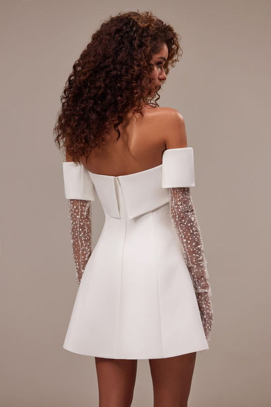 Showstopper mini wedding dress cut from satin. The sleeveless design features a straight neckline and a snatched waist that flows into a mini skirt. Can be complemented with an off-the-shoulder satin bolero with sheer long sleeves embellished with pearls.