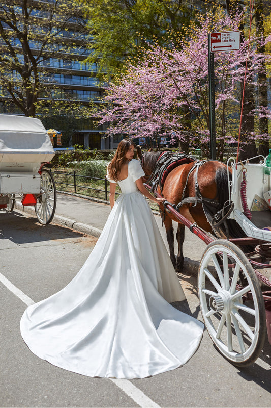 Gorgeous dress for a princess wedding look. The lush gown is made of glossy fabric and has no additional decorations. The corset is embellished with delicate Boat neckline and elbow-length loose sleeves with take-ups in the shoulders zone.